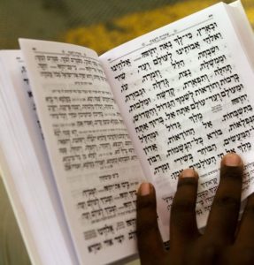 The hand of a Black Jewish person reading a prayer book in Hebrew